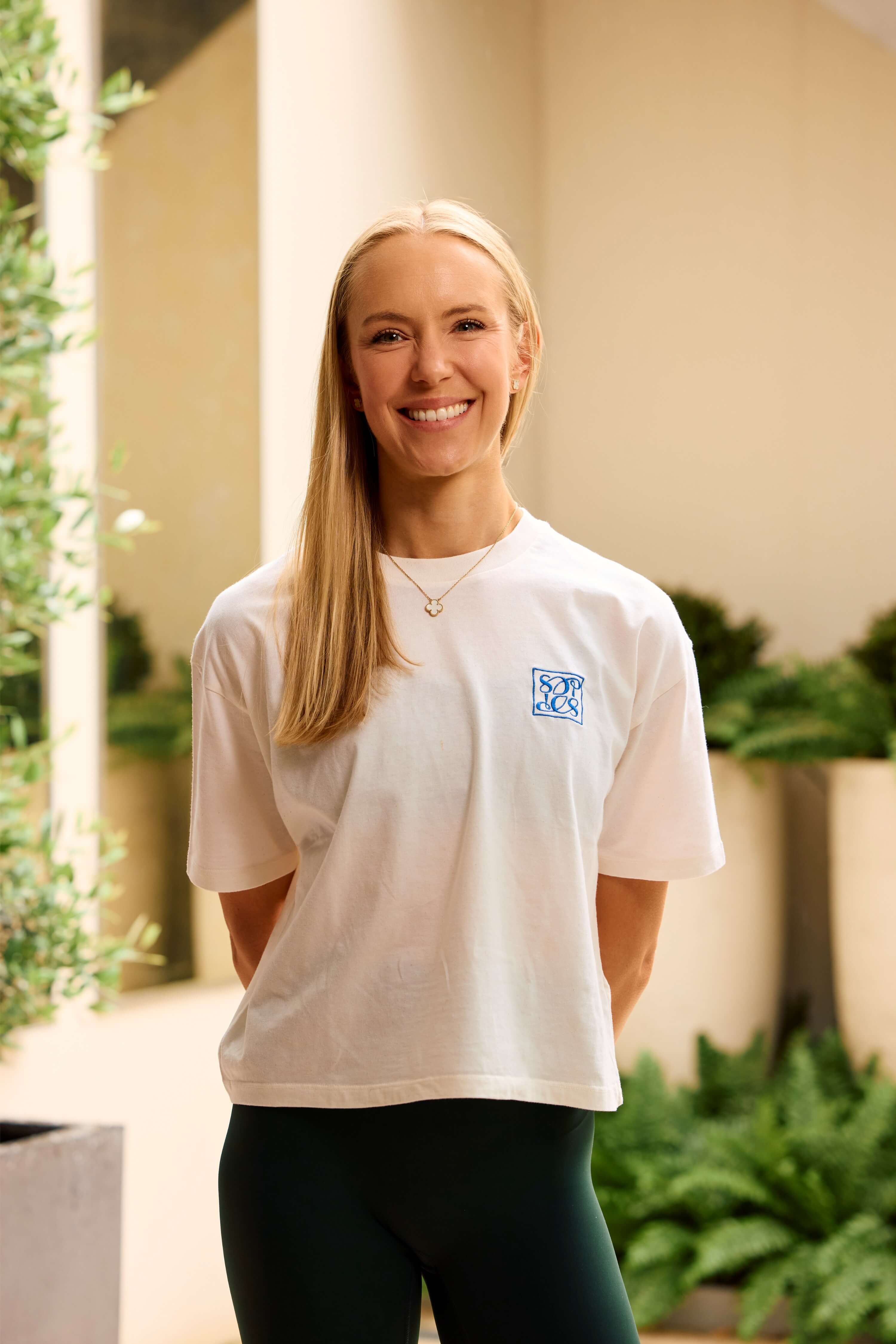 Sam Deville in her Wimbledon pilates studio smiling towards the camera where Sam Deville Pilates t-shirt .